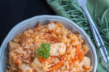 A bowl of Ukrainian chicken plov, rice pilaf, with a green cloth napkin and fork beside the bowl