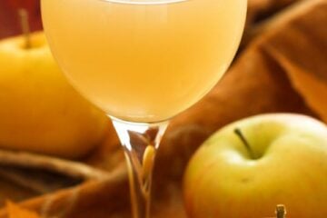 A wine glass with Russian apple kvas and full apples beside the glass