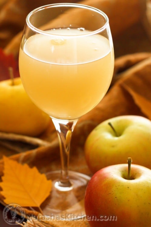 A glass of apple kvas standing on a cloth napkin with apples on it