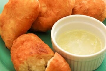 A green with Russian potato piroshki on it and a bowl of garlic dip