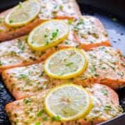four baked salmon fillets topped with lemon slices.