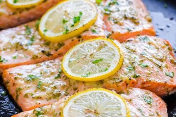 four baked salmon fillets topped with lemon slices.
