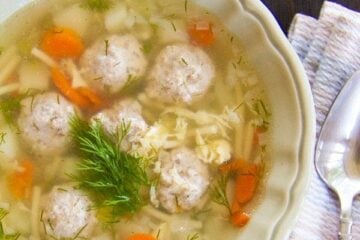 A bowl of mom's meatball soup with a cloth napkin and spoon beside it