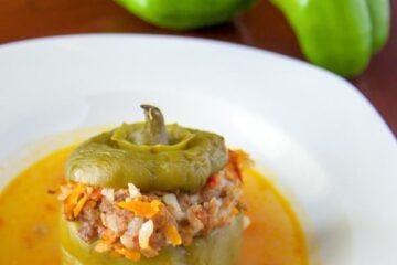 A plate of beef stuffed bell peppers with two raw green peppers behind the plate