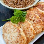 A plate of chicken kotleti lined up in a row with a bowl of buckwheat behind it