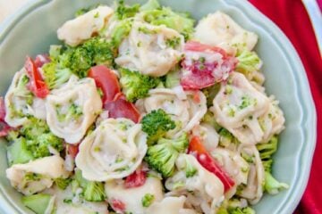 A bowl of tortellini salad with red, cloth napkin with a fork on top beside it
