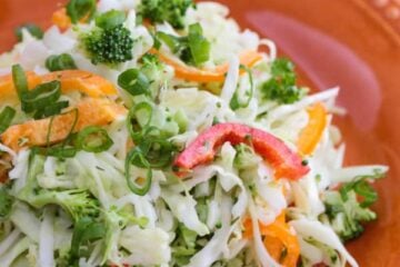 An orange plate with cabbage and bell pepper salad