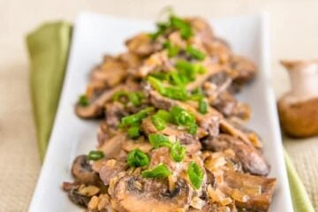 A long plate of mushrooms in a sour cream sauce garnished with green onions