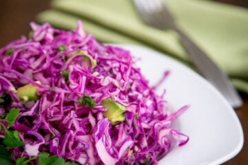 A plate of red cabbage and avocado salad with a fork and cloth napkin beside it