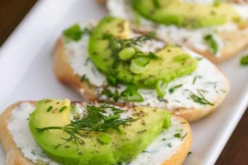 Four canap&eacute;s with garlic herb cream cheese and avocado in a roll on a plate