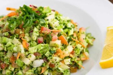 A bowl of loaded broccoli radish salad with a slice on lemon beside it