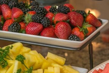 A three-tier tray with fruits such as pineapple, strawberries, and blackberries on it
