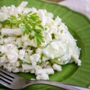 A green plate with cauliflower cucumber salad with a fork beside it