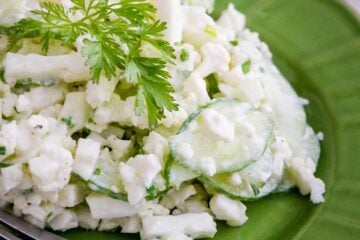A green plate with cauliflower cucumber salad with a fork beside it