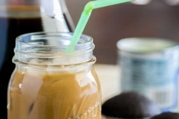 Iced coffee with condensed milk in a mason jar with a straw and cupcakes in the background