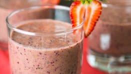 A glass of strawberry spinach smoothie garnished with a strawberry with more glasses in the background
