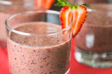 A glass of strawberry spinach smoothie garnished with a strawberry with more glasses in the background