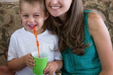 Natasha sitting at a table with her son with plates of food in front of them and her son is holding a cup