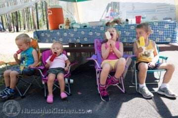 A group of young children sitting and eating ice cream with a picnic table behind them