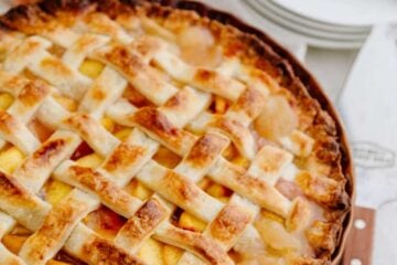 A peach pie with a spatula, plates, forks and fresh peaches beside it