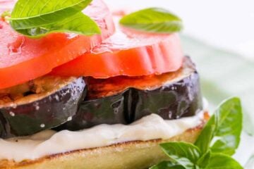 An open-faced eggplant and tomato sandwich garnished with basil on a green plate