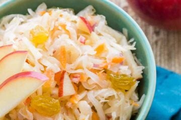 A green bowl of sauerkraut garnished with apples