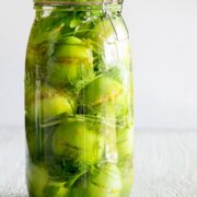 A clear glass jar with pickled stuffed green tomatoes