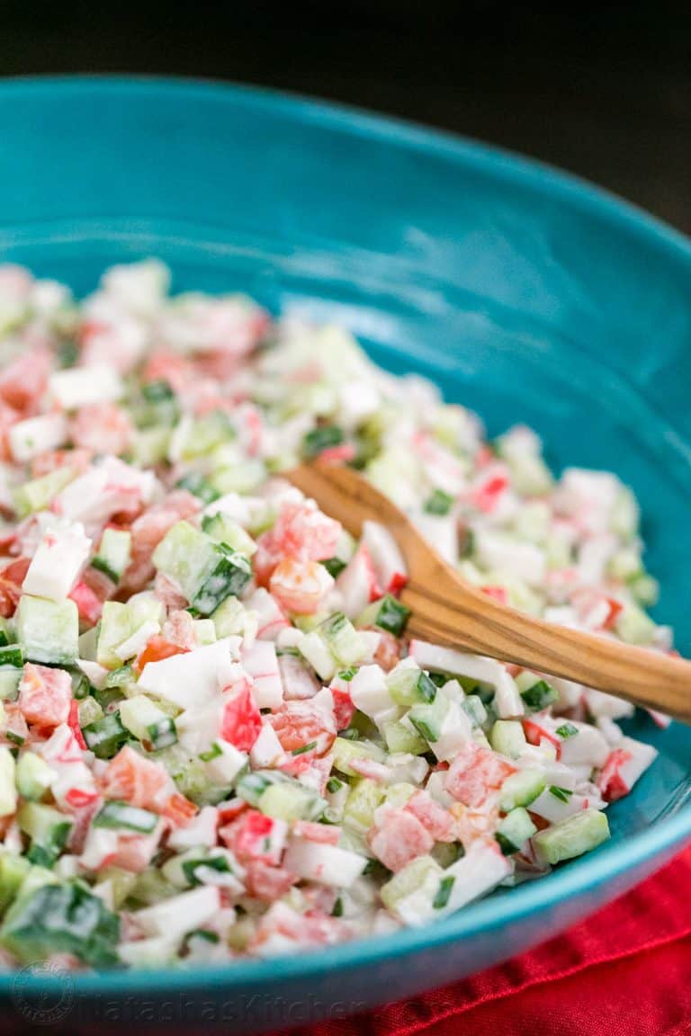 A blue bowl of crab salad with cucumber and tomato with a wooden spoon in it