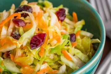 A close up of a green bowl of cabbage, carrot and cranberry salad