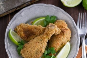 A plate of breaded baked chicken drumsticks garnished with lime wedges and cilantro