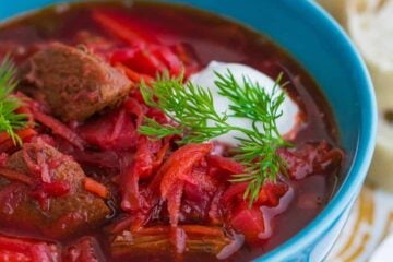 A bowl of borscht with meat garnished with sour cream and dill in a blue bowl