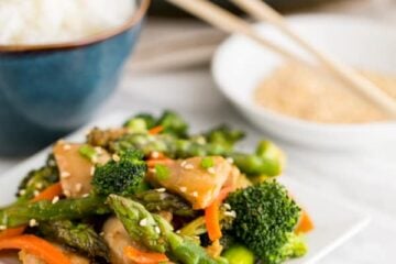 A plate of orange chicken and vegetable stir fry with a bowl of rice behind it