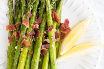 Roasted asparagus one a plate covered in bacon and lemon wedges on a plate