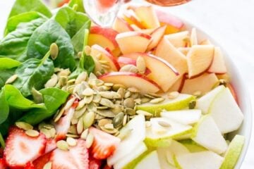 A fruit and spinach salad in a bowl with strawberry vinaigrette being poured on the salad