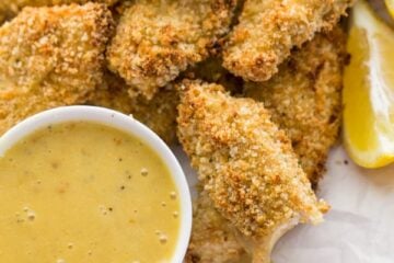 A plate of baked breaded chicken strips with a honey mustard dip beside them
