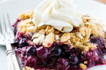 A plate and fork with a slice of blueberry crumble and whipped cream on it