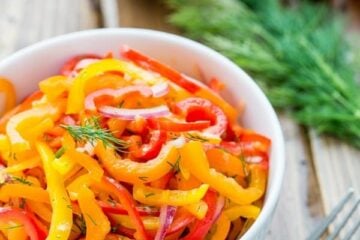 A bowl of zesty mini bell pepper salad with a fork, dill, mini peppers and purple onion beside it