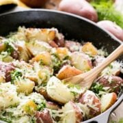 A skillet of buttered red potatoes garnished with parmesan and dill