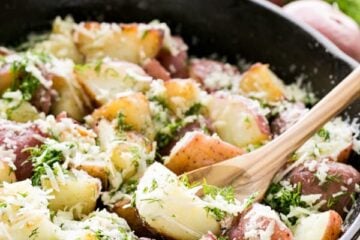 A skillet of buttered red potatoes garnished with parmesan and dill