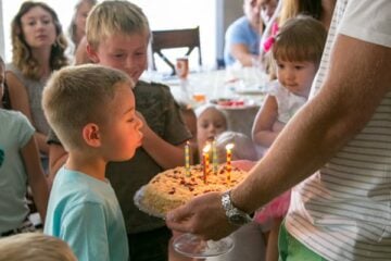 A group of children watching a boy blow out birthday candles on a cake held by his father