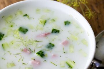 A bowl of Okroshka Summer Soup with dill and a spoon next to the bowl.