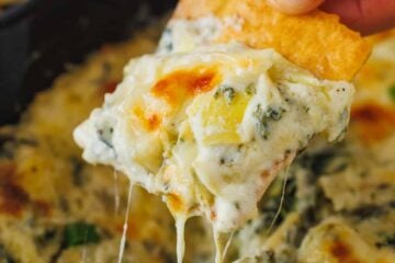 Cheesy spinach and artichoke dip scooped onto a chip with cheese pulls