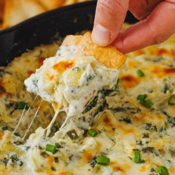 Cheesy spinach and artichoke dip scooped onto a chip with cheese pulls