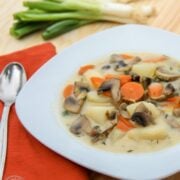 A bowl with Russian mushroom and potato soup with an orange, cloth napkin and spoon beside it