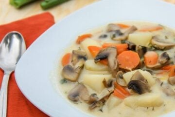 A bowl with Russian mushroom and potato soup with an orange, cloth napkin and spoon beside it