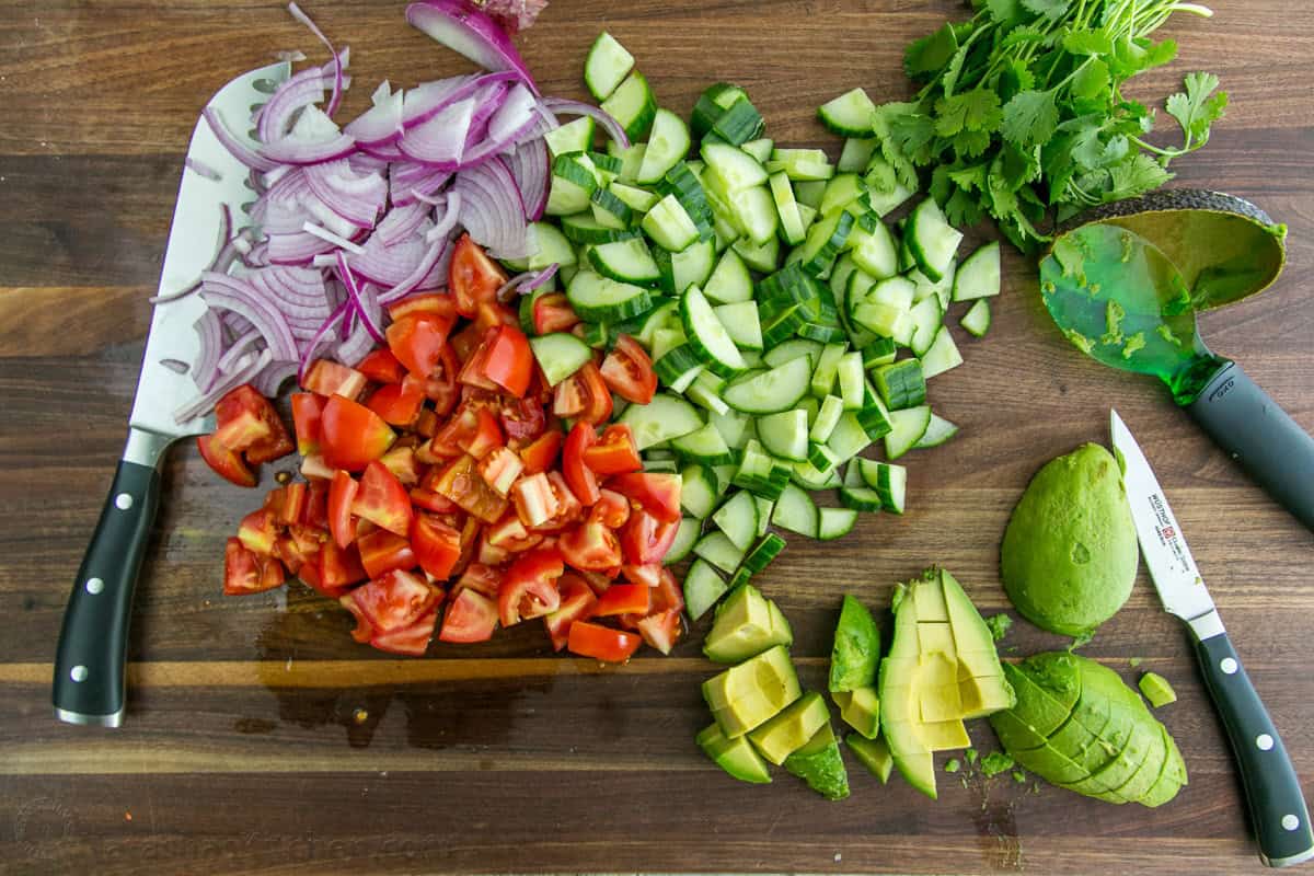 Chopped cucumbers, tomatoes and avocados on a cutting board.
