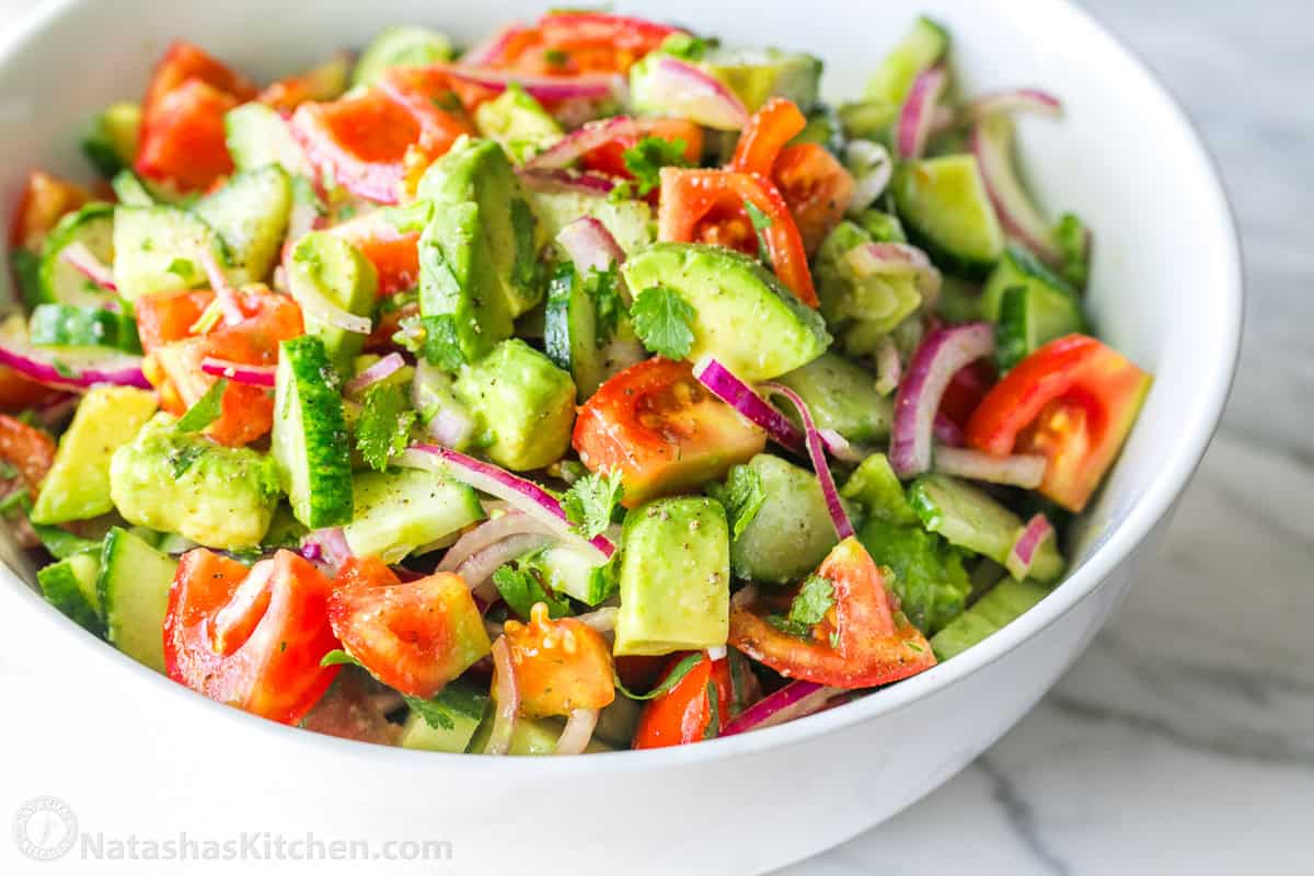 Cucumber tomato Avocado salad garnished with cilantro served in a white bowl