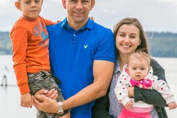Natasha and her family smiling at the camera with a  body of water behind them
