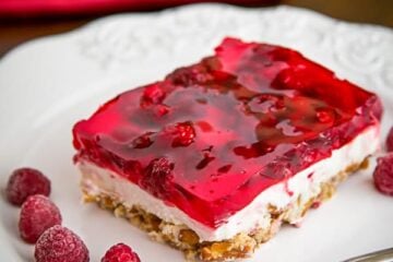 A slice of raspberry pretzel jello on a plate with raspberries beside it