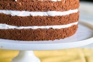 A close up of chocolate layer cake with creme chantilly frosting garnished with raspberries